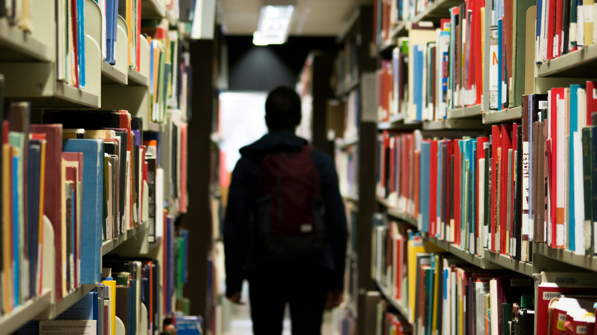 A student walking through bookshelves in a library.